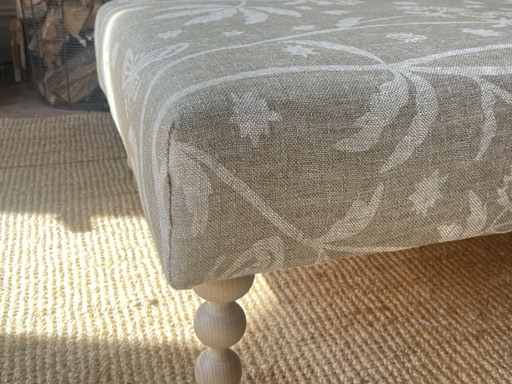 A turned wooden leg and the tailored corner of a linen cover, in low sunlight