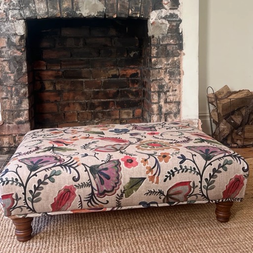 A floral-covered footstool in front of an open brick fireplace
